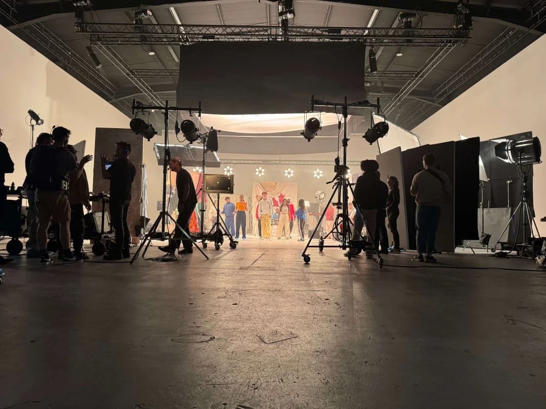 A film crew setting up lighting and camera equipment on a studio stage