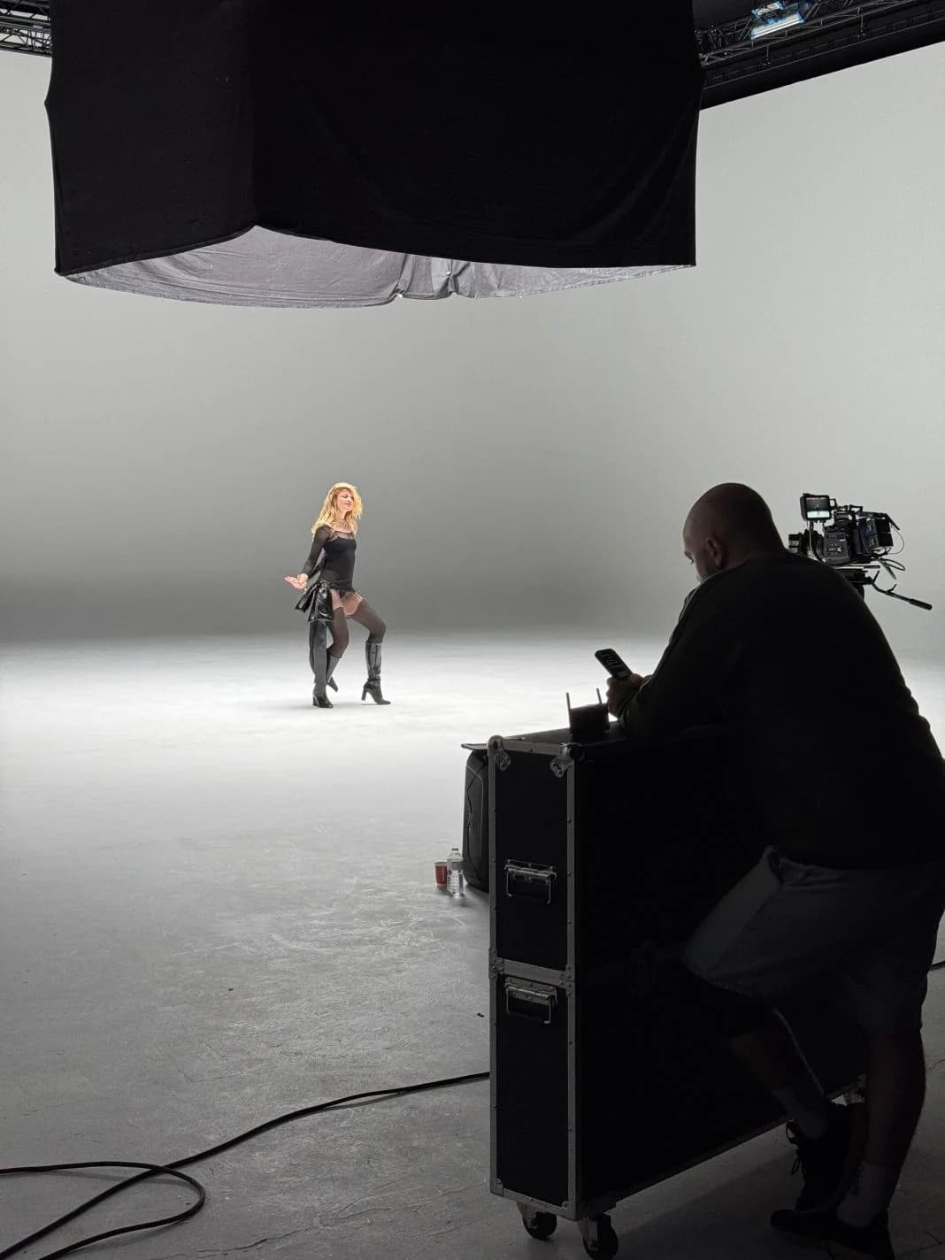 A performer on a white infinity cove stage while a crew member films