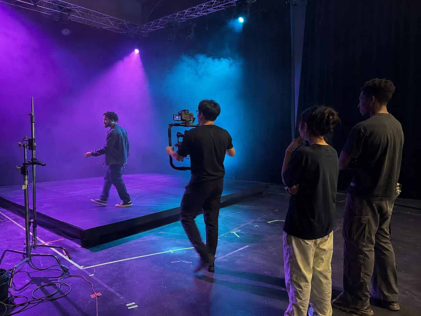 A performer on a black out stage with a smoke machine