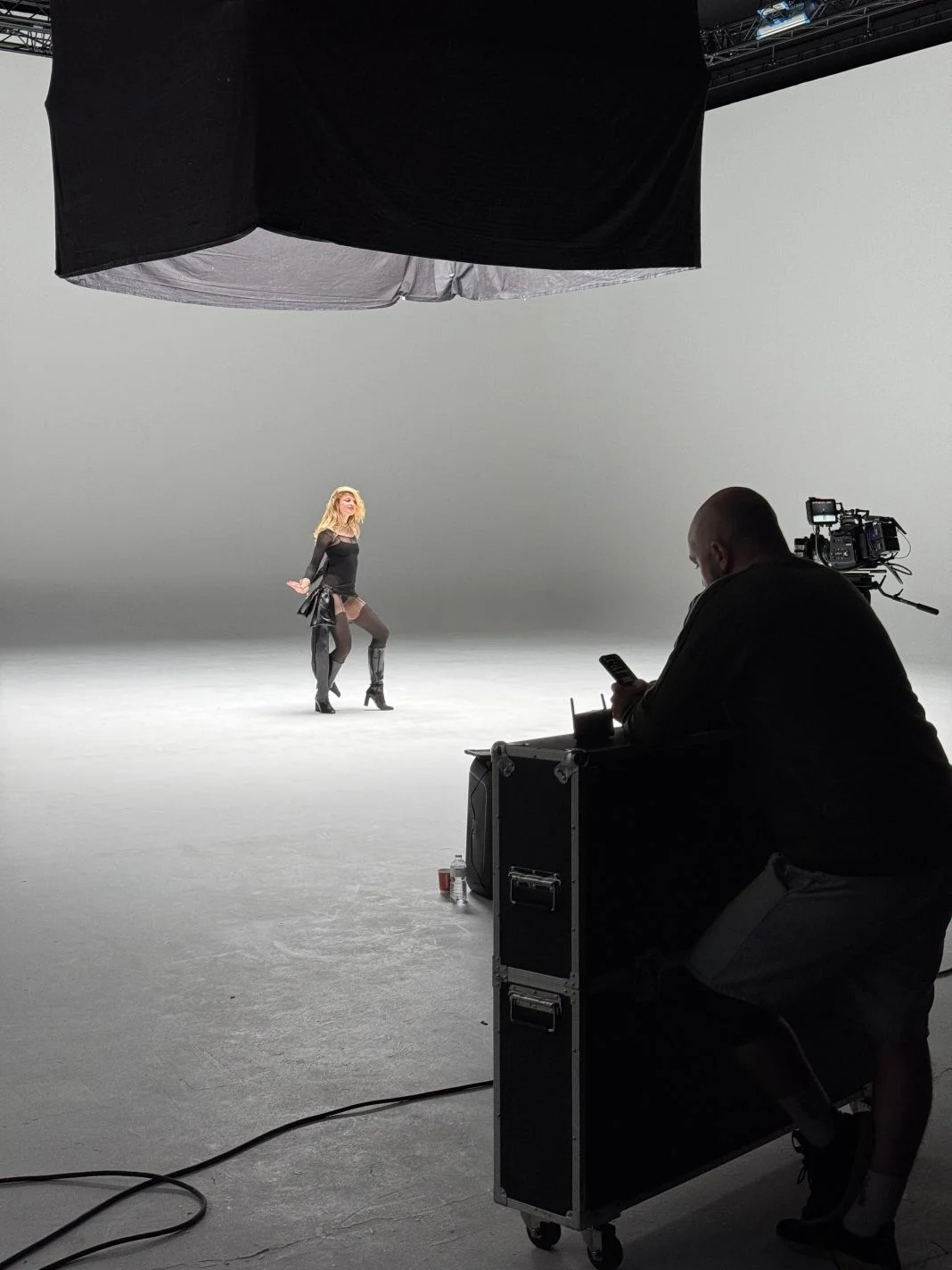 A performer on a white infinity cove stage while a crew member films