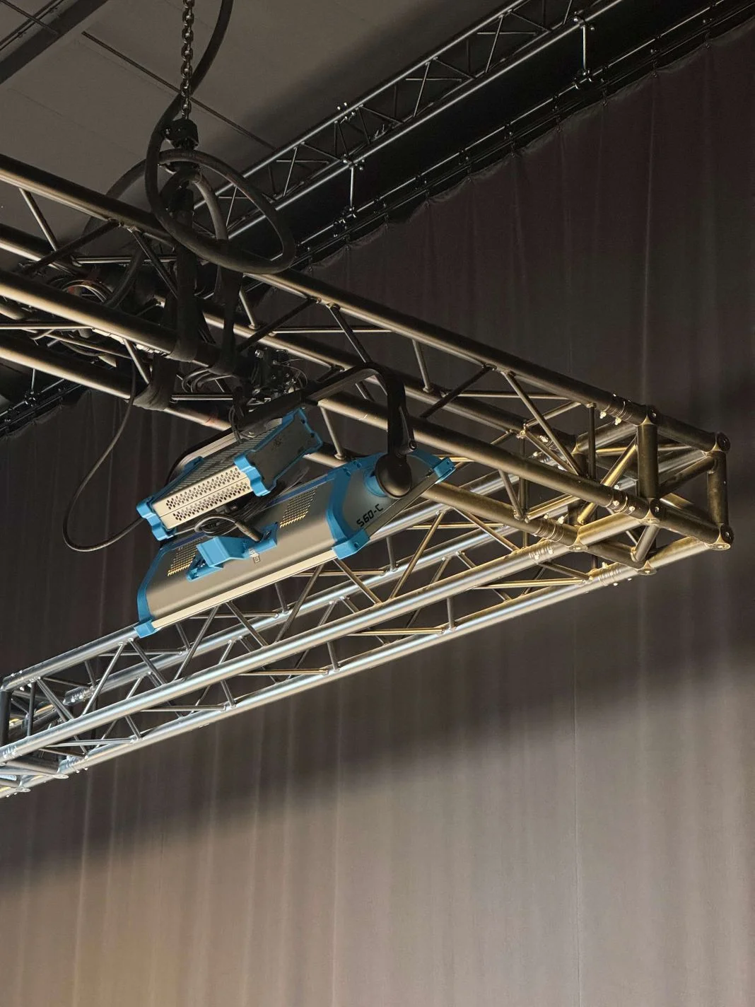 Stage lighting equipment suspended from a metal truss; cables hang above. The backdrop is a dark curtain. Text reads "560 C."