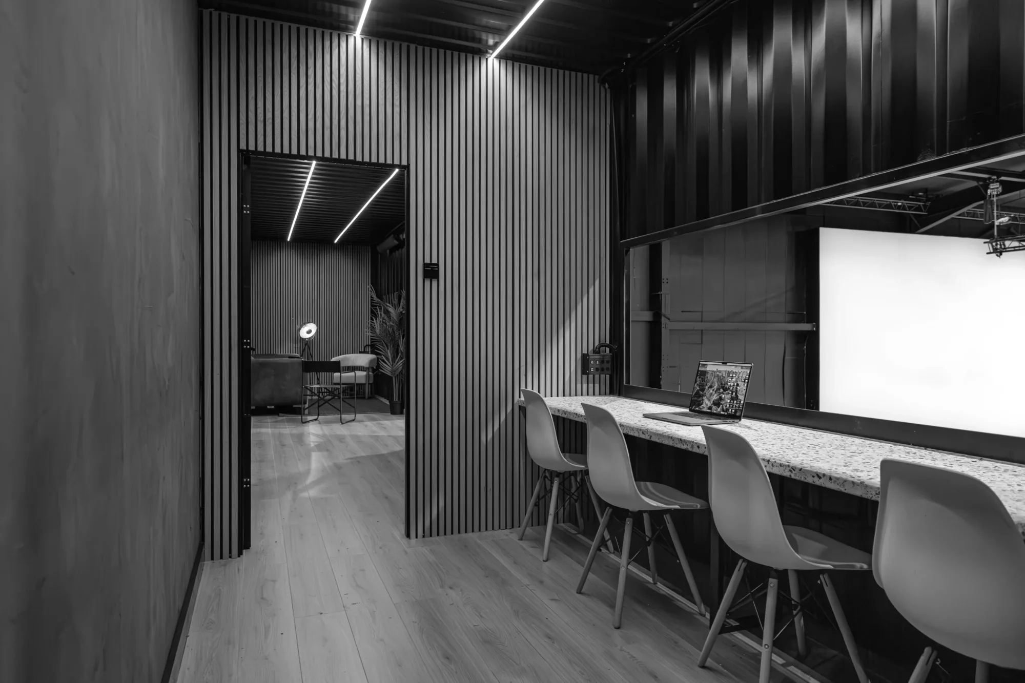 Modern interior with a hallway, striped walls, and chairs at a counter. A laptop is open on the counter. A light illuminates a back room.