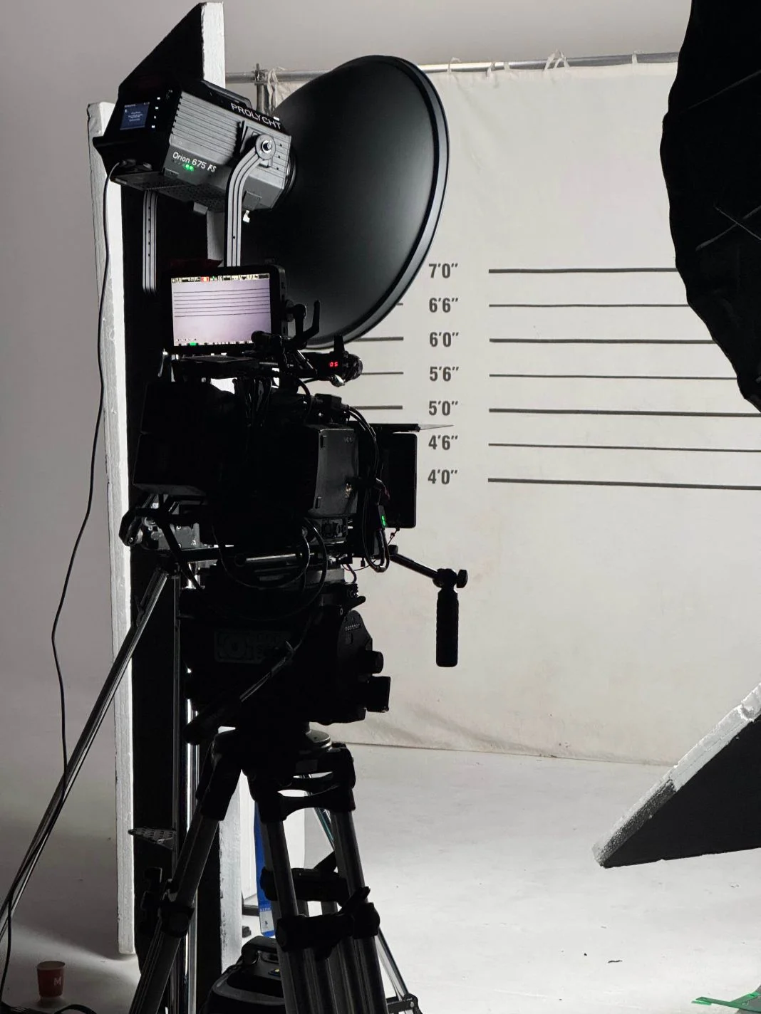 Film equipment set up in front of a height chart backdrop, showing measurements from 4’ to 7’. Studio setting with a tripod and lights.