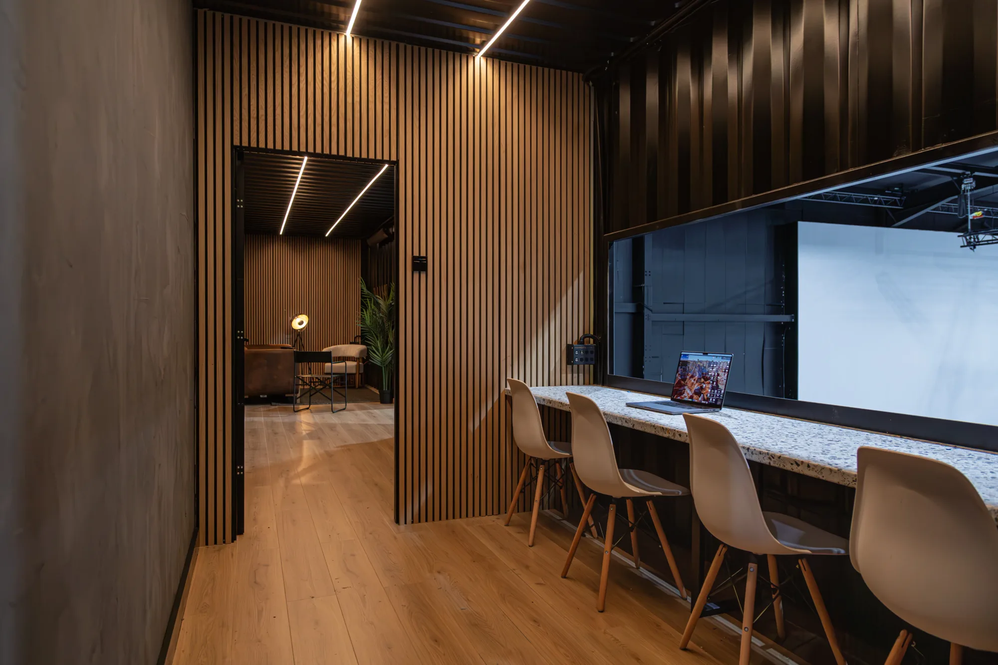Modern movie studio side office with wooden panelling, a laptop on a marble counter, and empty chairs. Soft lighting creates a sleek, minimalist vibe.
