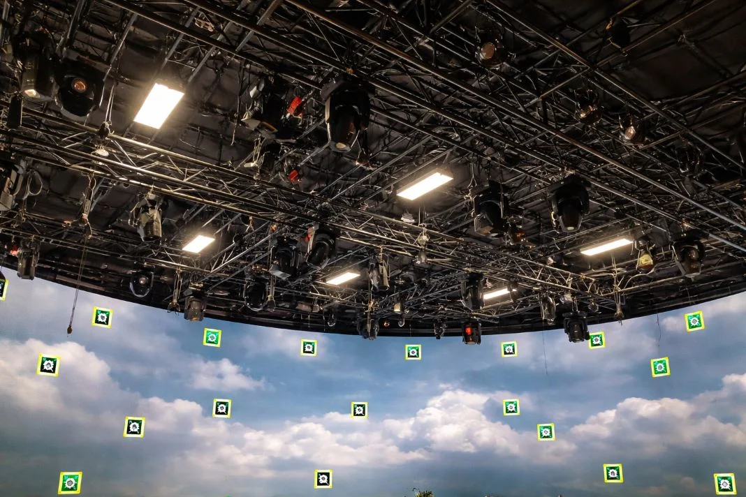 Studio ceiling with numerous stage lights and cables, sky backdrop with clouds below, marked by green and yellow symbols.