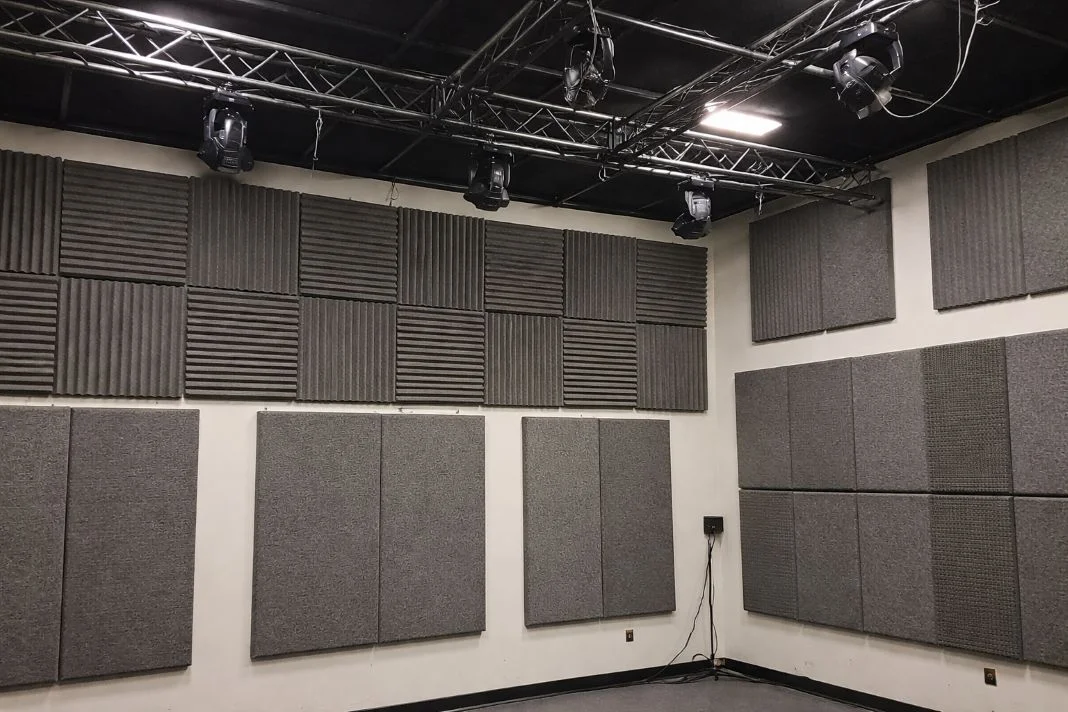 Soundproof room with gray acoustic panels on walls. Ceiling has black lights and metal trusses. Neutral and calm environment.