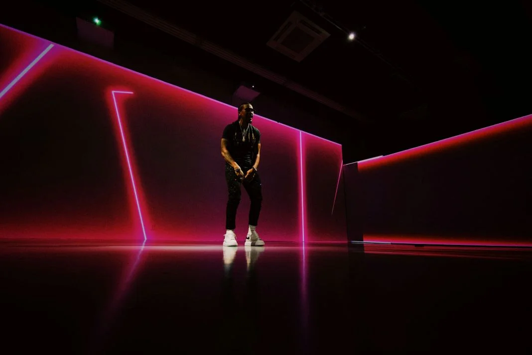 Person in dark room with neon pink and purple lights, standing on a reflective floor. Mood is dynamic and futuristic.