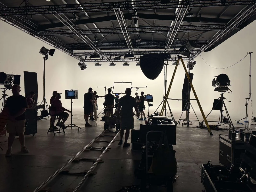Silhouetted film crew in a studio setting with cameras and lighting equipment. Focused, professional mood with a plain white backdrop.